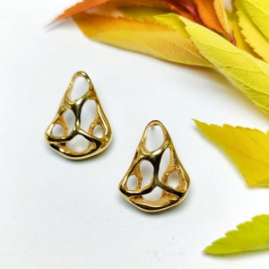 May include: A pair of gold-toned earrings with a geometric, openwork design. The earrings are shaped like a teardrop and have a delicate, intricate pattern.