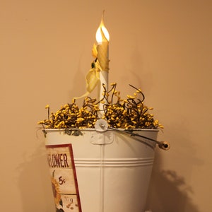 May include: A white metal bucket with a sunflower design and a decorative candle. The bucket is filled with yellow berries and has a handle. The candle has a yellow and white patterned design.