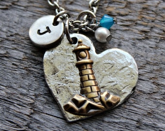 May include: Silver necklace with a heart charm featuring a gold lighthouse, a silver charm with the letter J, a white pearl bead, and a blue glass bead.
