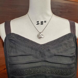 May include: A silver necklace with a round pendant featuring a tree design. The necklace is 18 inches long.