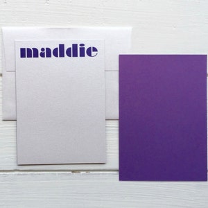 May include: A white card with a purple envelope and a purple card. The white card has the word "maddie" printed in blue letters.