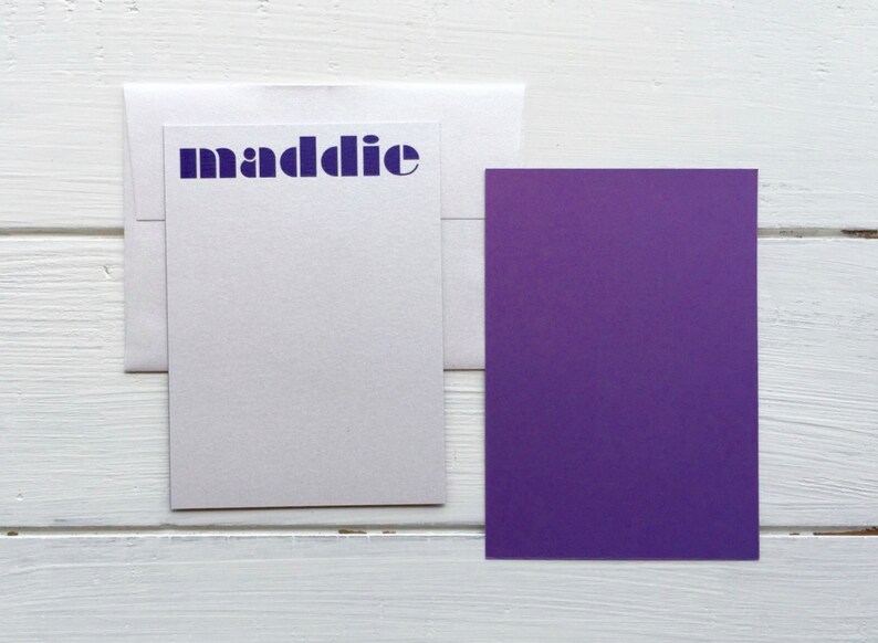 May include: A white card with a purple envelope and a purple card. The white card has the word "maddie" printed in blue letters.