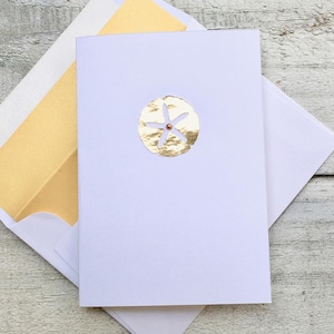 May include: A white card with a gold foil cutout of a sand dollar. The sand dollar has a five-pointed star in the center.