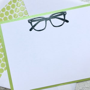 May include: A white card with a green border and a black and white illustration of a pair of eyeglasses.
