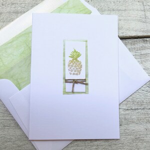 May include: A white card with a green and yellow pineapple illustration inside a green frame. The frame is tied with a brown twine bow.