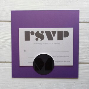 May include: A white RSVP card with black text that reads "rsvp" and "Kindly reply by the 10th of January". There are two lines below the text for the guest to check "M" for attending or "regret this decision" for not attending. A black circle with a white "M" inside is on the card.