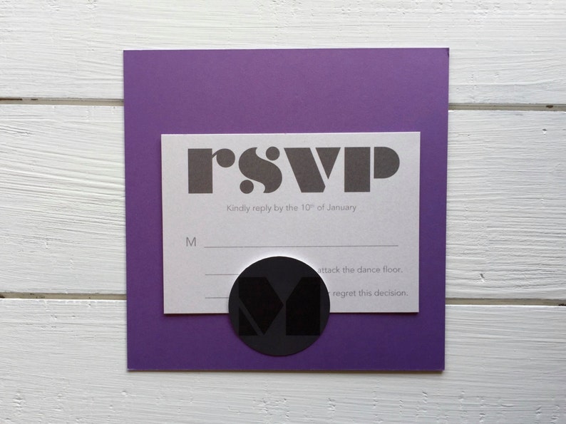 May include: A white RSVP card with black text that reads "rsvp" and "Kindly reply by the 10th of January". There are two lines below the text for the guest to check "M" for attending or "regret this decision" for not attending. A black circle with a white "M" inside is on the card.