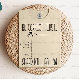 May include: A beige t-shirt with the text "BE CORRECT FIRST... SPEED WILL FOLLOW" printed on it. The text is in black and includes a simple diagram of a circle with arrows and letters.