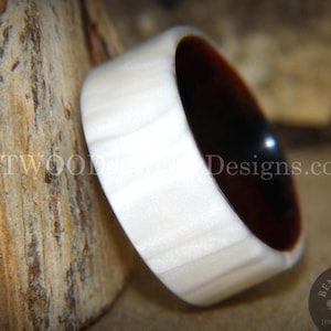 May include: A handcrafted wooden ring with a light-colored exterior and a dark brown interior. The ring is set against a textured, light brown background. The website address "BentwoodJewelryDesigns.com" is visible.