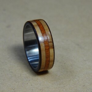 May include: A wooden ring with a stainless steel band. The wood is a light brown with darker brown stripes.