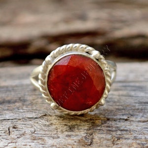 Può includere: Un anello d'argento con una pietra preziosa rossa incastonata in una fascia d'argento intrecciata.