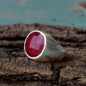 Può includere: Un anello d'argento con una grande pietra rotonda di colore rosso.