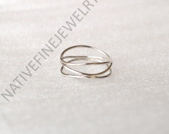 May include: A silver ring with a distinctive, open design. The ring has three intersecting bands, creating a striking, modern appearance. The ring is made of a shiny, metallic material.