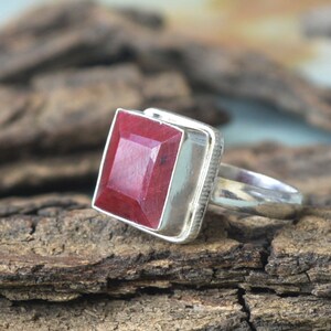 Könnte beinhalten: Ein silberner Ring mit einem großen, quadratischen, roten Edelstein. Der Ring ist in einer schlichten, silbernen Fassung gefasst.