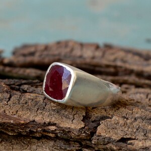 May include: A silver ring with a square-shaped red gemstone.
