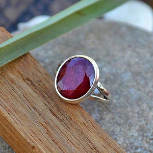 Peut inclure: Une bague en argent avec une grande pierre précieuse en rubis de forme ovale. Le rubis est de couleur rouge foncé et a une taille facetée. La bague est sertie dans une simple bande en argent.