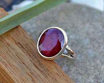 Op de afbeelding: Een zilveren ring met een grote, ovale robijn. De robijn is diep rood van kleur en heeft een facetgeslepen vorm. De ring is gezet in een eenvoudige, zilveren band.
