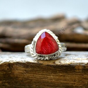 Può includere: Un anello d'argento con una pietra preziosa rossa triangolare incastonata in una fascia d'argento intrecciata.