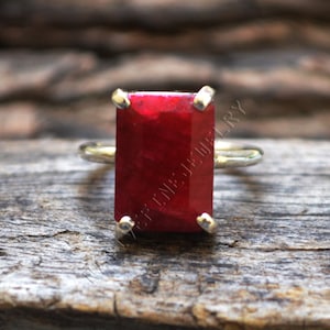 May include: A silver ring with a large, rectangular, red gemstone. The ring is set on a wooden surface.