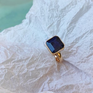 May include: A gold ring with a square, dark blue gemstone.