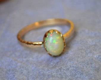 Könnte beinhalten: Ein zarter Goldring mit einem weißen Opal-Edelstein, der in einer gewellten Fassung sitzt.