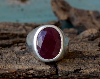 Op de afbeelding: Een zilveren ring met een grote, ovale, gefacetteerde robijn-edelsteen, gezet in een bezel-setting.