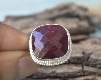 May include: A silver ring with a large, faceted, red ruby gemstone. The ring has a decorative, twisted silver band.