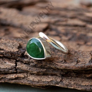 May include: A silver ring with a green gemstone. The ring is a simple band with a teardrop-shaped stone set in the center.