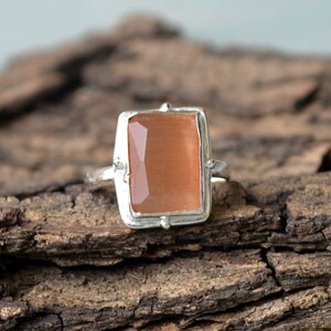 May include: A silver ring featuring a rectangular, peach-coloured gemstone set in a bezel setting.