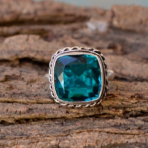 Peut inclure: Une bague en argent avec une grande pierre précieuse carrée bleu turquoise sertie dans une bélière en argent décorative.