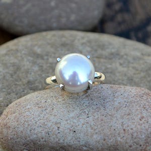 May include: A silver ring featuring a large, white pearl set in a four-prong setting.