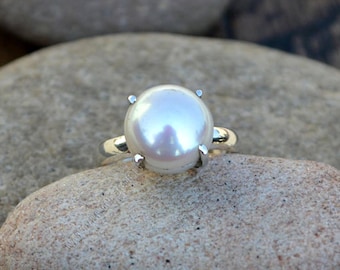 May include: A silver ring with a large, white pearl set in a four-prong setting.