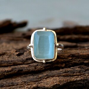 May include: A silver ring with a light blue gemstone. The gemstone is a rectangular shape with rounded corners and is set in a silver bezel.