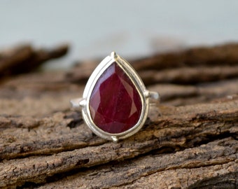 May include: A teardrop-shaped ruby gemstone ring set in sterling silver. The ring features a deep red ruby with a faceted cut and a silver band.