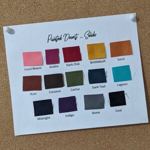 May include: A colour chart of fabric swatches with names such as Coral Bloom, Azalea, Dark Chili, Brittlebush, Sand, Rust, Coconut, Cactus, Dark Teal, Lagoon, Midnight, Indigo, Stone, and Coal. The chart is titled "Painted Desert - Solids".