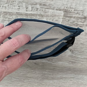 May include: A teal blue zippered pouch with a clear plastic window. The pouch has a black strap.