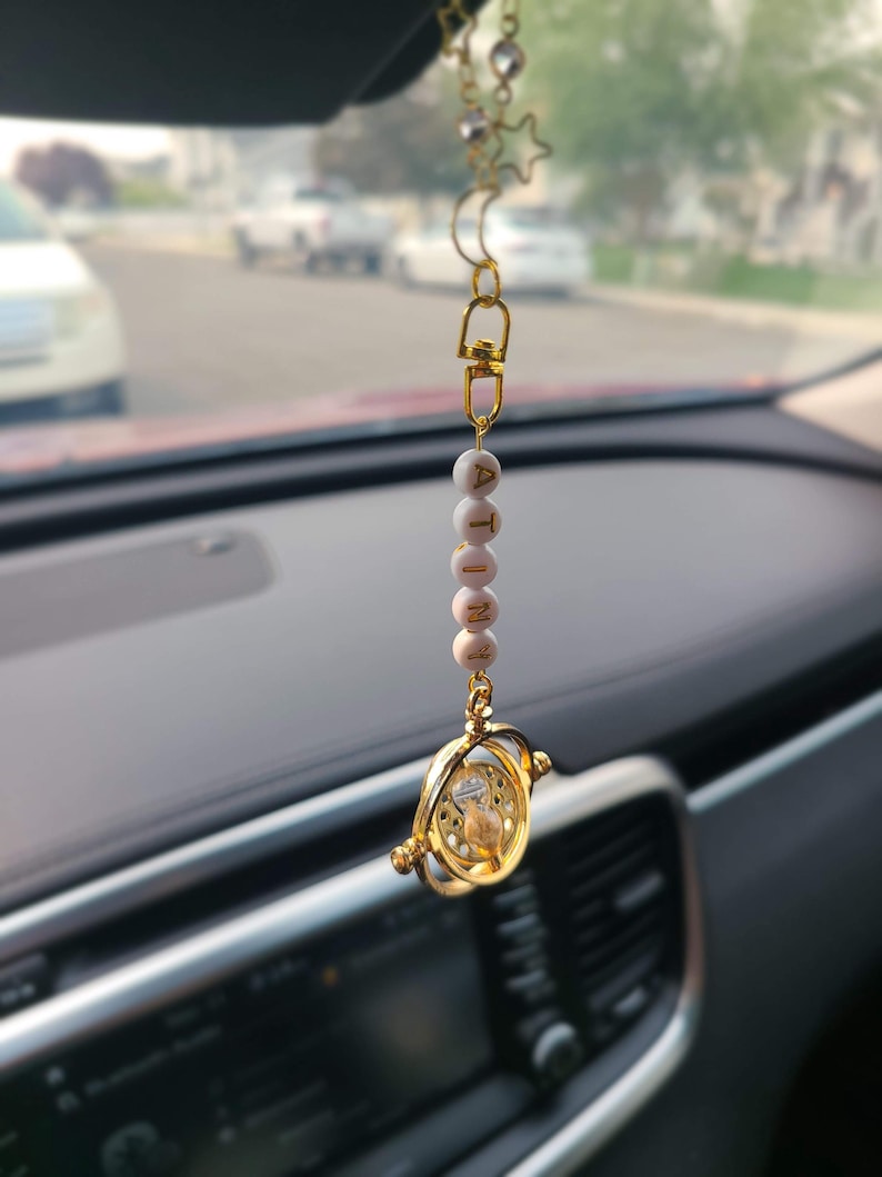 May include: Gold car charm with a small hourglass and a beaded chain with the word "ATINY" spelled out in white beads.