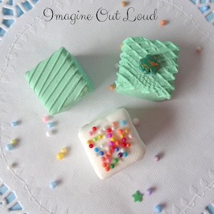 May include: Three small square cakes decorated with green frosting. One cake has a green leaf design, one has a diagonal striped design, and one has colorful sprinkles.