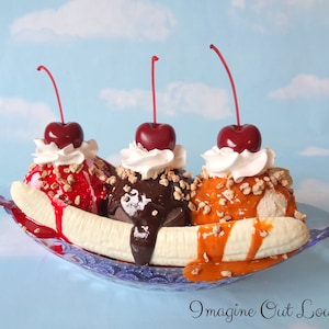 May include: A banana split sundae with three scoops of ice cream, topped with whipped cream, cherries, nuts, and chocolate sauce. The sundae is served in a glass dish with a blue and white pattern.