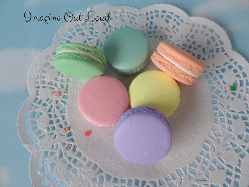 May include: Five pastel-colored macarons on a white doily. The macarons are green, blue, pink, yellow, and purple.