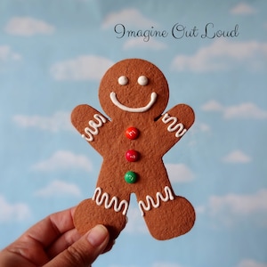 Può includere: Un biscotto di pan di zenzero a forma di uomo decorato con glassa bianca e un viso sorridente. Il biscotto ha tre M&M's sul suo torso, uno rosso, uno arancione e uno verde. Il biscotto è tenuto in una mano su uno sfondo blu e bianco nuvoloso. Il testo "Imagine Out Loud" è scritto in nero nella parte superiore dell'immagine.