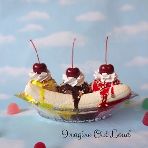 May include: A banana split sundae with three scoops of ice cream, topped with whipped cream, cherries, and chocolate sauce. The sundae is in a glass dish with a banana on top. There are gummy sweets scattered around the dish.