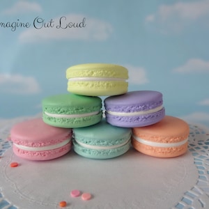 May include: A stack of six pastel-colored macarons with white filling. The macarons are arranged in a pyramid shape on a white doily with colorful sprinkles.