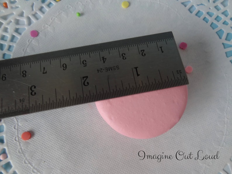 May include: A pink circle measuring 2 inches in diameter, with a ruler placed on top of it. The ruler is marked with inches and has the text "SSME-24" printed on it.