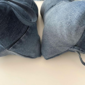 May include: Two denim fabric bags with handles. The bags are made of blue denim material and have a rounded shape. The bags are placed side by side on a white surface.