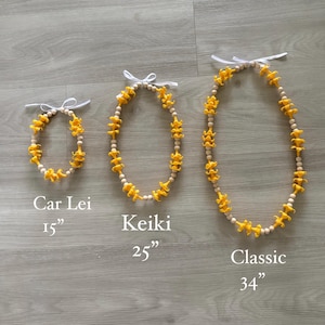 May include: Three leis of varying sizes, each featuring yellow flower-shaped beads and wooden beads. The leis are labeled "Car Lei" (15 inches), "Keiki" (25 inches), and "Classic" (34 inches). Each lei has a white ribbon tie.