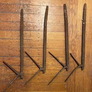 May include: Five rusty metal fireplace tools with a pointed end and a forked end. The tools are arranged in a row on a wooden surface.
