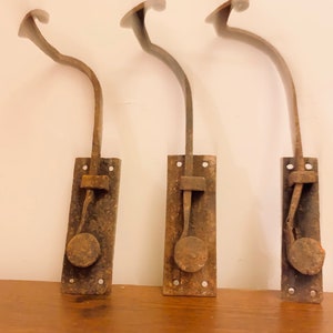 May include: Three antique metal door latches with a curved arm and a round knob. The latches are rusty and have a worn, aged appearance.