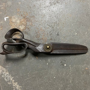 May include: A vintage pair of metal shears with a brass rivet. The shears have a long blade and a double-loop handle.