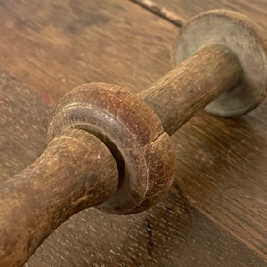 May include: A close-up of a wooden spool with a smooth, worn surface. The spool has a round shape with a hole in the center. The wood is a light brown color with darker brown streaks.